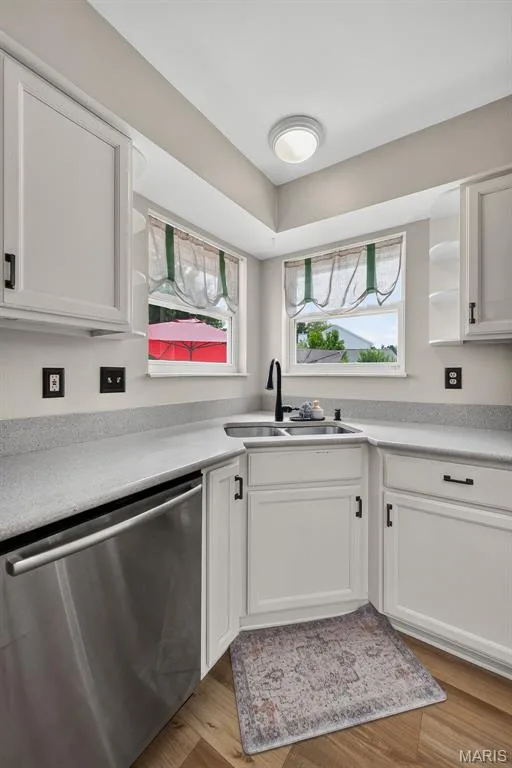 White cabinetry, stainless steel dishwasher, corner sink with black faucet, light grey countertops, and wood-finish flooring — 10 Docs Ct., St Charles, MO 63303