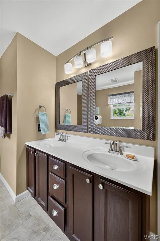 Dual sink vanity with dark wood-finish cabinetry, white integrated sinks, and brushed nickel hardware — 10 Docs Ct., St Charles, MO 63303