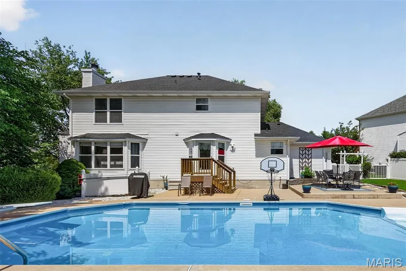 Expansive backyard featuring a built-in swimming pool, a concrete patio, and a wooden deck with stairs — 10 Docs Ct., St Charles, MO 63303