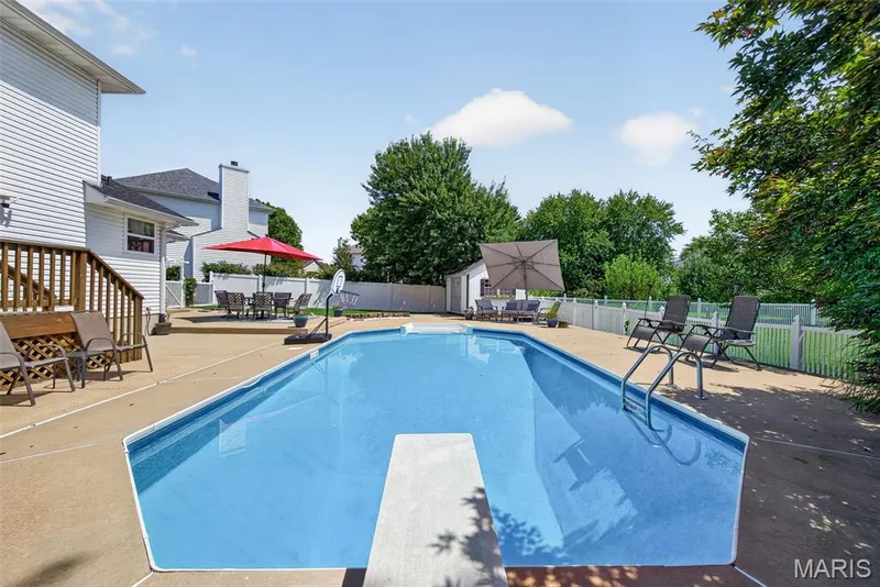 Expansive concrete patio surrounding a built-in swimming pool with a diving board and entry ladder — 10 Docs Ct., St Charles, MO 63303
