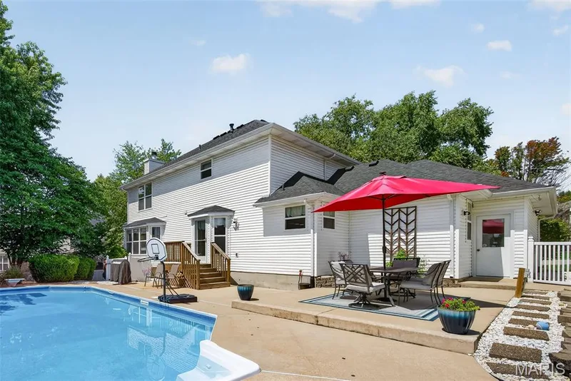 Outdoor swimming pool with concrete surround, wood deck with stairs, white siding exterior, and a paved patio area — 10 Docs Ct., St Charles, MO 63303