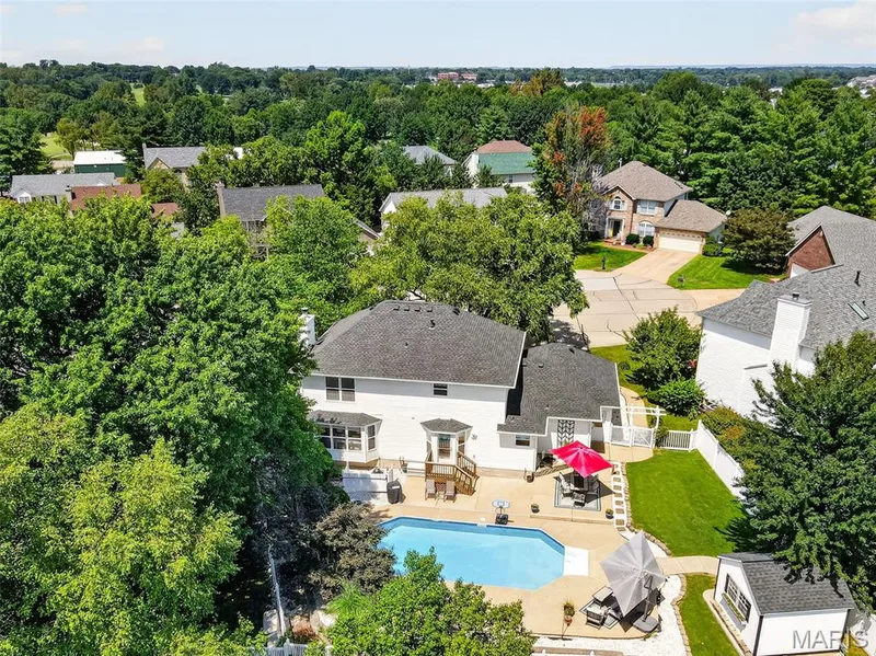 Expansive backyard featuring a blue-tiled swimming pool, concrete patio, and a white shed — 10 Docs Ct., St Charles, MO 63303