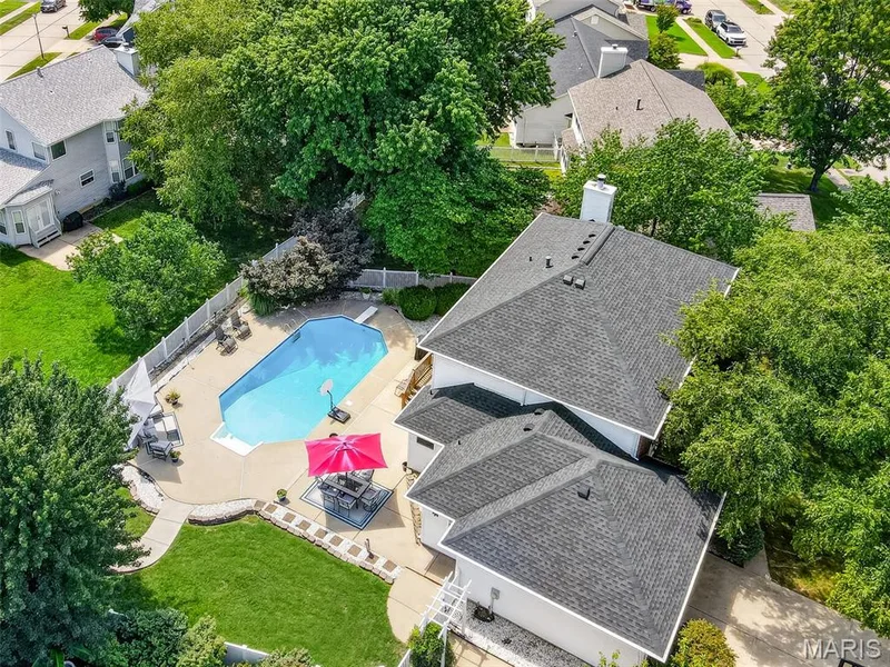 Expansive backyard featuring an in-ground pool, concrete patio, white privacy fence, and mature trees — 10 Docs Ct., St Charles, MO 63303