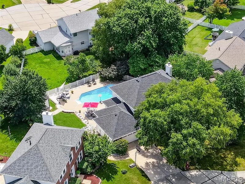 In-ground pool, expansive concrete patio, lush green lawn, mature trees, and privacy fencing — 10 Docs Ct., St Charles, MO 63303