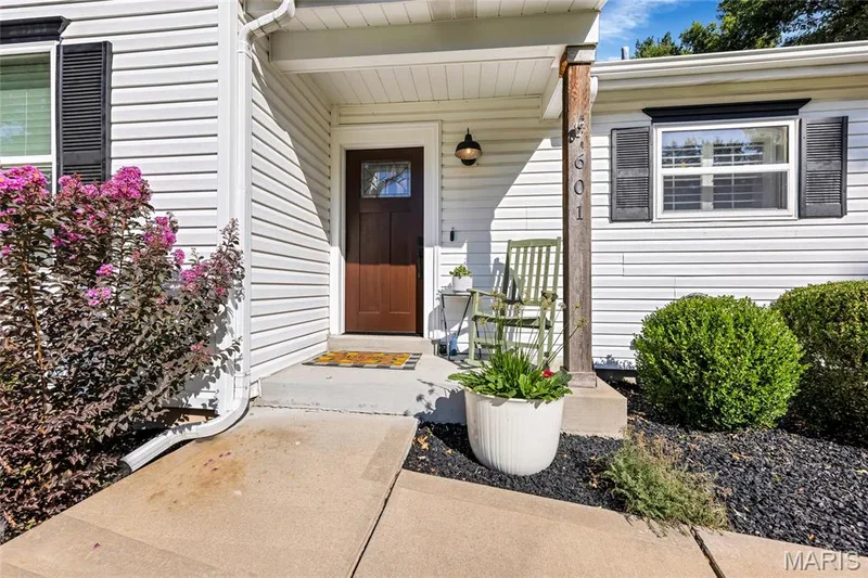White siding exterior with black shutters, a covered entry, a dark wood-finish front door with an integrated window, and a concrete pathway — 601 Big Timber Lane, O'Fallon, MO 63368