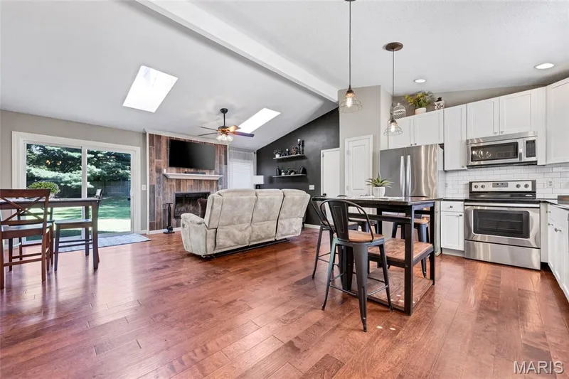 Vaulted ceiling with skylights, wood-finish flooring, white cabinetry, stainless steel appliances, and a sliding glass door to the exterior — 601 Big Timber Lane, O'Fallon, MO 63368