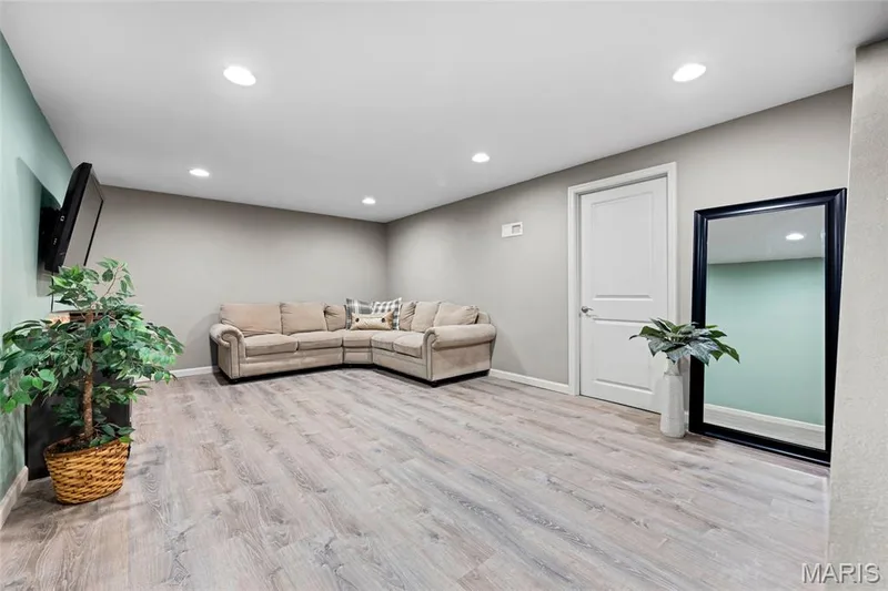 Sleek recessed lighting and fresh, light wood floors make this basement family room feel incredibly bright, polished, and cozy—a perfectly scaled setup for a snug lounge, media nook, or play space — 601 Big Timber Lane, O'Fallon, MO 63368