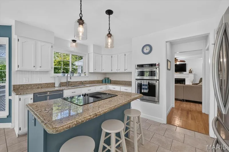 Kitchen featuring white cabinetry, granite countertops, a central island with an integrated cooktop, double wall ovens, and tile flooring — 5856 Canterfield Court, Weldon Spring, MO 63304