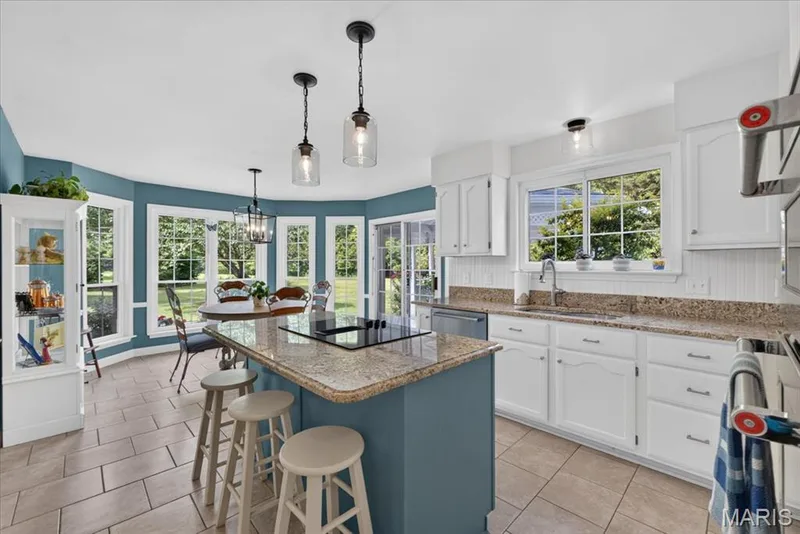 Kitchen featuring an island with cooktop, granite countertops, white cabinetry, tile flooring, and multiple windows — 5856 Canterfield Court, Weldon Spring, MO 63304