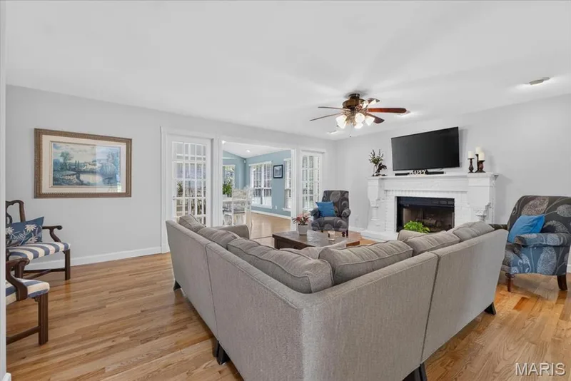 Hardwood flooring, painted brick fireplace with mantel, ceiling fan with integrated lighting, and French doors — 5856 Canterfield Court, Weldon Spring, MO 63304