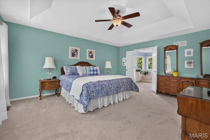 Tray ceiling, light-toned carpeting, ceiling fan, and double doors opening to an adjoining room with a built-in tub — 5856 Canterfield Court, Weldon Spring, MO 63304