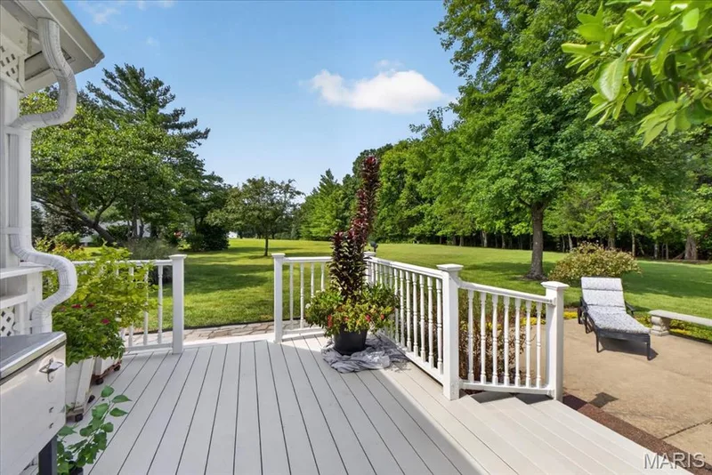 Expansive outdoor deck with a white railing system, leading to a concrete patio and a large grassy area with mature trees — 5856 Canterfield Court, Weldon Spring, MO 63304