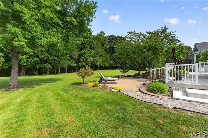 Expansive lawn area with mature trees, stone patio, composite deck with white railings, and curved stone pathway — 5856 Canterfield Court, Weldon Spring, MO 63304