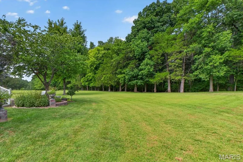 Expansive lawn space featuring mature trees and a bordered garden bed — 5856 Canterfield Court, Weldon Spring, MO 63304