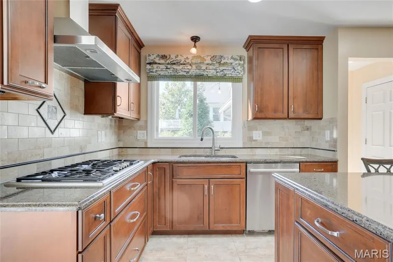 Wood-finish cabinetry, stainless steel range hood, built-in gas cooktop, stone countertops, and tile backsplash — 2508 Peppermill Lake Court, Chesterfield, MO 63005