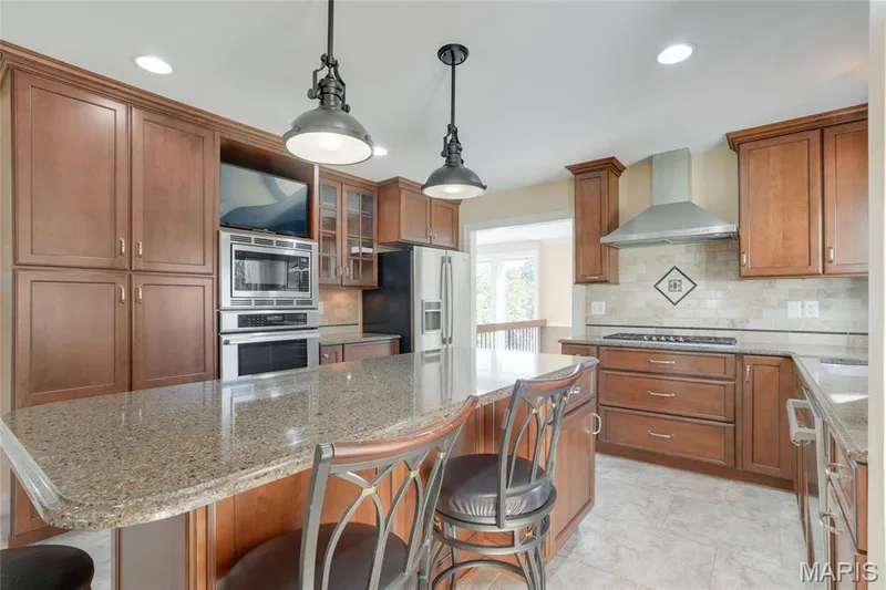 Kitchen featuring wood cabinetry, granite countertops, stainless steel appliances, a tiled backsplash with decorative inlay, and pendant lighting — 2508 Peppermill Lake Court, Chesterfield, MO 63005