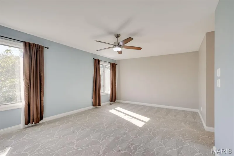 Patterned carpeting, two windows, two-tone wall paint, and a ceiling fan with integrated lighting — 2508 Peppermill Lake Court, Chesterfield, MO 63005