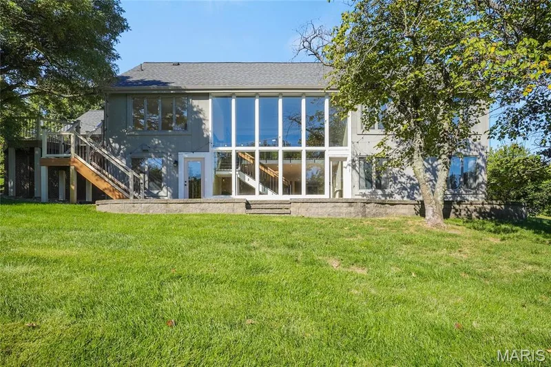 Expansive rear exterior featuring a wall of floor-to-ceiling windows, a ground-level patio, and a raised composite deck with stairs — 2508 Peppermill Lake Court, Chesterfield, MO 63005