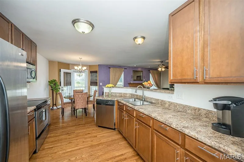 Kitchen featuring wood cabinetry, stainless steel appliances, a double basin sink, and wood-finish flooring — 500 Flowering Magnolia Drive, O'Fallon, MO 63366