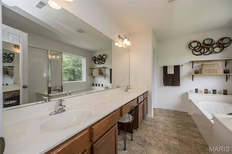 Dual vanity with integral sinks, expansive counter space, wood-finish cabinetry, built-in soaking tub, and tiled flooring — 500 Flowering Magnolia Drive, O'Fallon, MO 63366