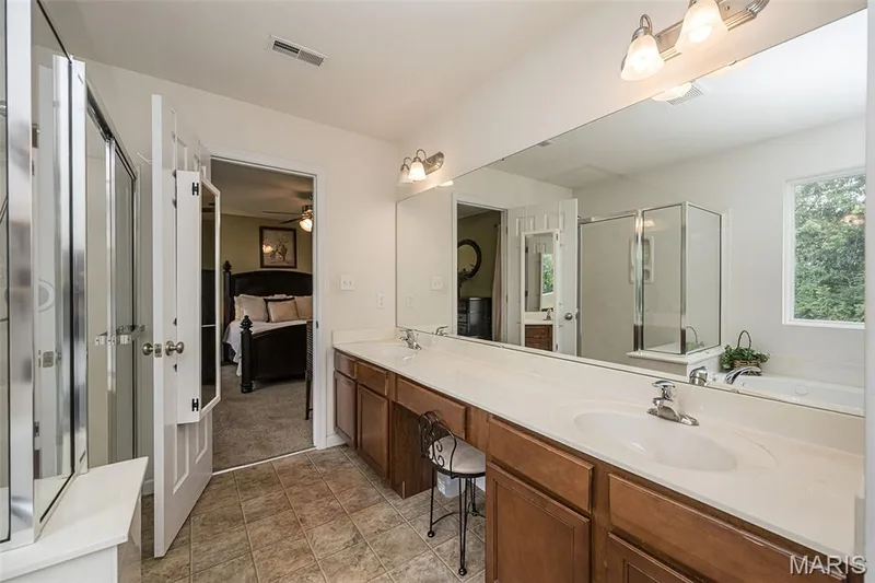 Dual sink vanity with wood-finish cabinetry and an expansive wall-mounted mirror — 500 Flowering Magnolia Drive, O'Fallon, MO 63366