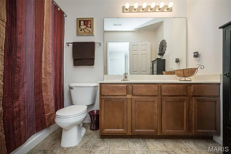 Bathroom featuring a vanity with a white countertop and wood-finish cabinetry, a large wall-mounted mirror, and tile flooring — 500 Flowering Magnolia Drive, O'Fallon, MO 63366