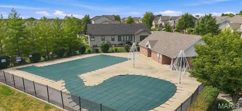 Expansive outdoor pool area with surrounding concrete decking, secured by black metal fencing, and featuring a brick-clad pool house — 500 Flowering Magnolia Drive, O'Fallon, MO 63366