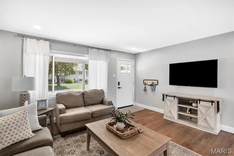 Recessed lighting, wood-finish flooring, white paneled entry door with glass inserts, wall-mounted television, and a media console with sliding barn-style doors — 7 Saint Mark Drive, St Peters, MO 63376