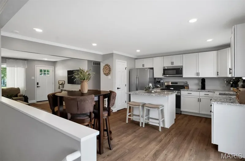 Kitchen featuring white cabinetry, stainless steel appliances, a center island with seating, granite countertops, and wood-finish flooring — 7 Saint Mark Drive, St Peters, MO 63376