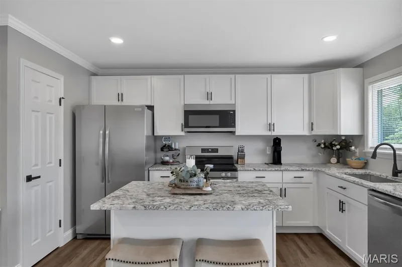 Kitchen featuring white shaker cabinetry, stainless steel appliances, a center island with countertop seating, and wood-finish flooring — 7 Saint Mark Drive, St Peters, MO 63376