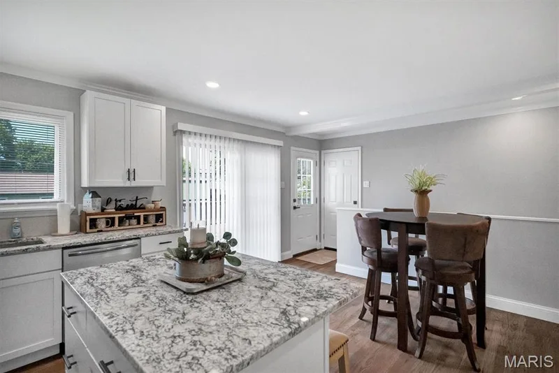 Kitchen featuring white cabinetry, a large kitchen island with a light-toned countertop, stainless steel appliances, and wood-finish flooring — 7 Saint Mark Drive, St Peters, MO 63376