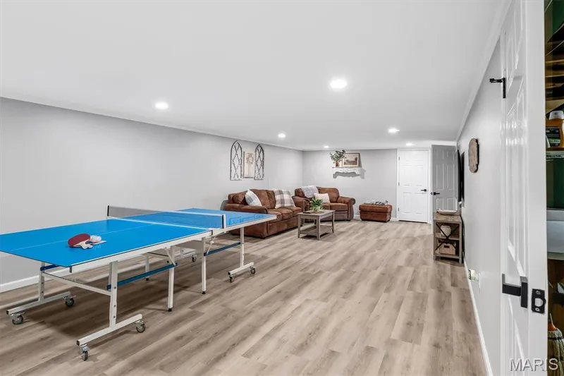 Recessed lighting illuminates wood-finish flooring throughout this expansive lower level, featuring light gray walls and a white door — 7 Saint Mark Drive, St Peters, MO 63376