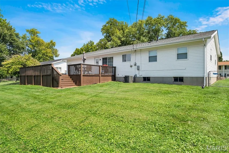 Expansive backyard featuring a manicured lawn, a large wood-finish deck with railings, and white siding — 7 Saint Mark Drive, St Peters, MO 63376