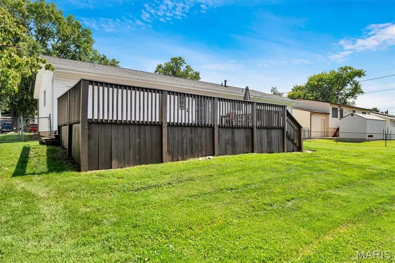 Expansive backyard with a wooden deck featuring vertical slat railing and a privacy lattice base — 7 Saint Mark Drive, St Peters, MO 63376