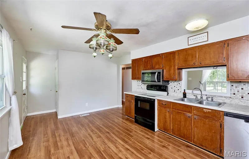 Kitchen featuring wood-finish flooring, wood cabinetry, stainless steel appliances, and a mosaic tile backsplash — 318 Capri Drive, O'Fallon, MO 63366