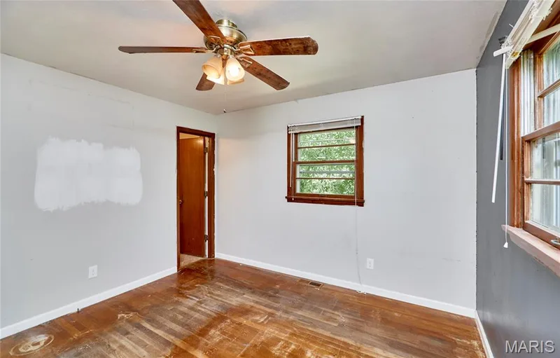 Bright bedroom showcasing hardwood flooring, ceiling fan with integrated lighting, and natural light from transom window — 318 Capri Drive, O'Fallon, MO 63366