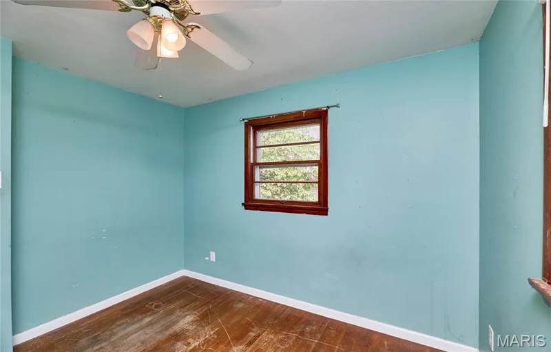 Wood-finish flooring, single window with wood trim, ceiling fan with light fixture, and light blue wall finish — 318 Capri Drive, O'Fallon, MO 63366