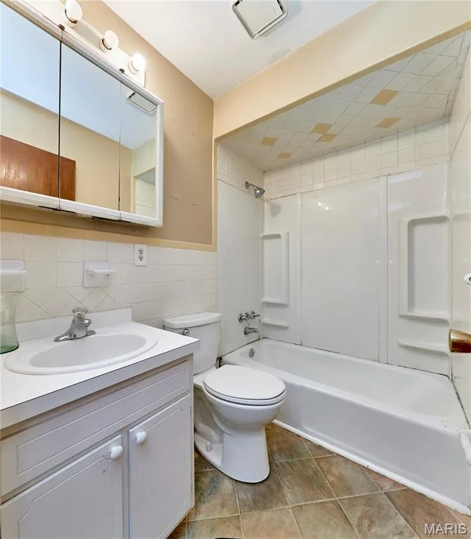 Bathroom featuring a white vanity with integrated sink, white tiled walls, a shower/tub combination, and tiled flooring — 318 Capri Drive, O'Fallon, MO 63366
