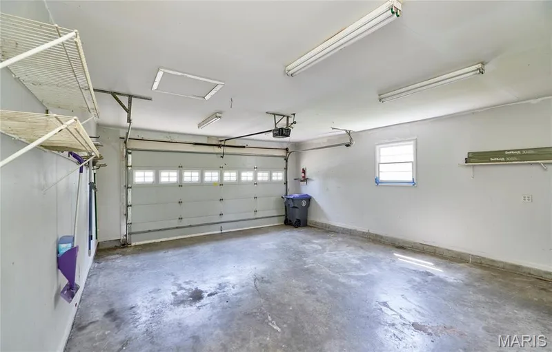 Attached garage with a concrete floor, overhead lighting, and built-in shelving — 318 Capri Drive, O'Fallon, MO 63366