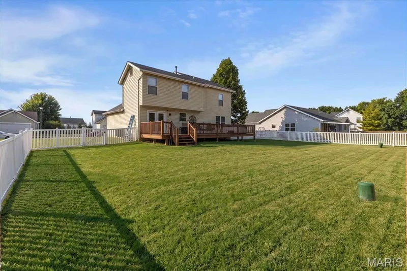 Spacious backyard featuring a manicured lawn, white picket fencing, and a multi-level wood deck — 35 Snowmass Court, O'Fallon, MO 63368