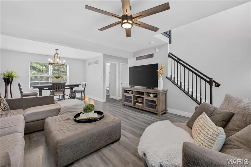 Open-concept living space featuring wood-finish flooring, a modern ceiling fan, and a staircase with black metal balusters — 35 Snowmass Court, O'Fallon, MO 63368
