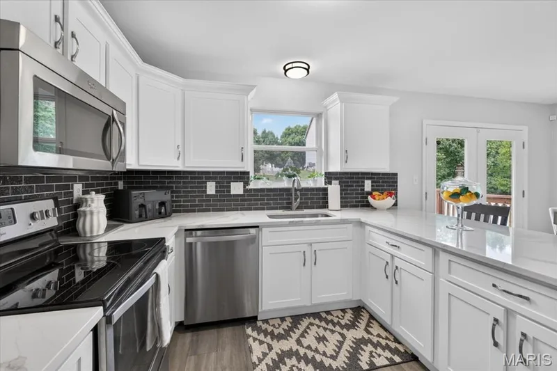 Kitchen featuring white cabinetry, stainless steel appliances, white countertops, a black subway tile backsplash, and wood-finish flooring — 35 Snowmass Court, O'Fallon, MO 63368