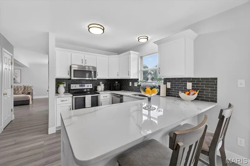 White cabinetry, stainless steel appliances, black subway tile backsplash, white countertops, and wood-finish flooring — 35 Snowmass Court, O'Fallon, MO 63368