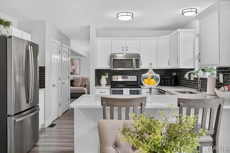 Modern kitchen featuring white cabinetry, stainless steel appliances, dark subway tile backsplash, and light-toned countertops — 35 Snowmass Court, O'Fallon, MO 63368