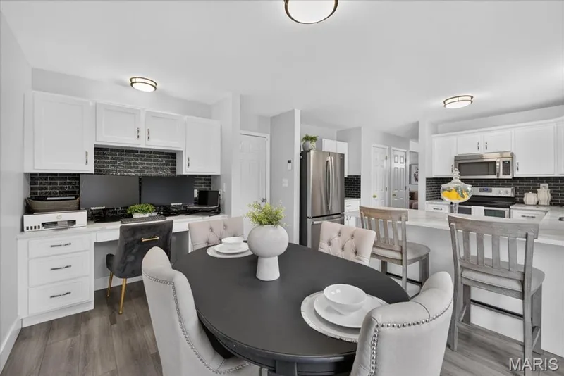 White cabinetry with black subway tile backsplash, stainless steel appliances, and wood-finish flooring — 35 Snowmass Court, O'Fallon, MO 63368