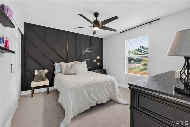 Accent wall with geometric paneling, ceiling fan with integrated lighting, window with blinds, and light-colored carpeting — 35 Snowmass Court, O'Fallon, MO 63368