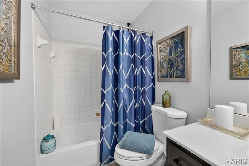 Bathtub with white subway tile surround, polished chrome shower rod, white toilet, and dark wood-finish vanity with white countertop — 35 Snowmass Court, O'Fallon, MO 63368