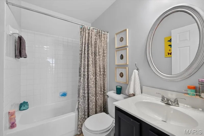 White subway tile shower surround with a built-in tub, a dark wood-finish vanity with an integrated sink, a silver-framed oval mirror, and a toilet — 35 Snowmass Court, O'Fallon, MO 63368