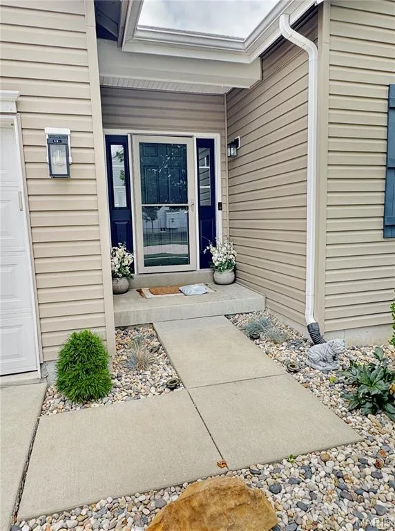 Front entry with concrete walkway, light-toned siding, and exterior lighting fixtures — 4024 Glengarry Drive, Wentzville, MO 63385