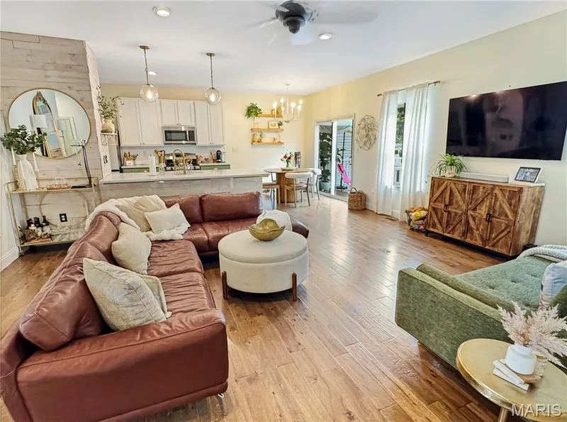 Open-concept living area featuring wood-finish flooring, a ceiling fan, white kitchen cabinetry, and sliding glass doors — 4024 Glengarry Drive, Wentzville, MO 63385